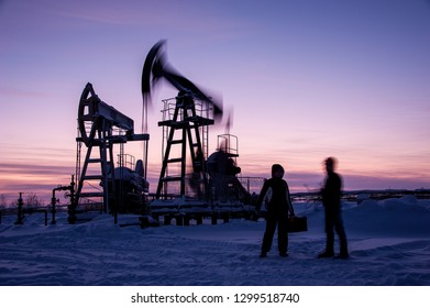 Oil Workers In Oilfield. Pump Jack And Engineer On A Winter Sunset Sky Background. Western Siberia.