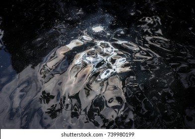 Oily Black Pond Water With Ripples And Reflections From Sky And Foliage. Glistening Water Background Texture.