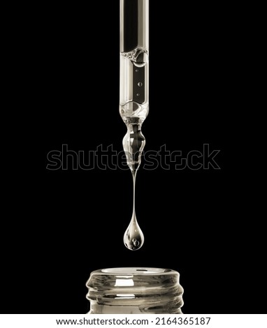 Oily drop dripping from pipette into cosmetic bottle close up on a black background