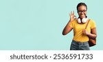 Okay. African Student Lady Gesturing Ok Sign Posing With Backpack Smiling To Camera Over Blue Background. Studio Shot