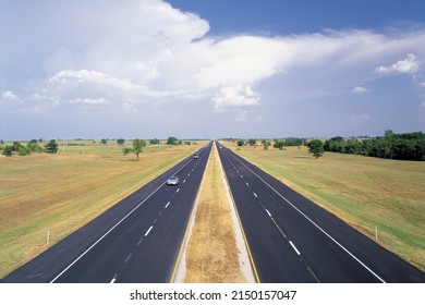 Oklahoma, USA - July 1, 2006: High Angle View Of Cars Driving On Straight Asphalt Road With Wide Center Line Surrounded By Grassland Against Cumulus In The Sky
