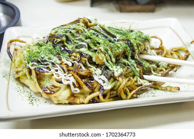 Okonomiyaki Dish. Japanese Street Food Meal With Chopsticks. Fried Ingredients With Noodle Pasta. Declicious Foodie Travel Tour Background.