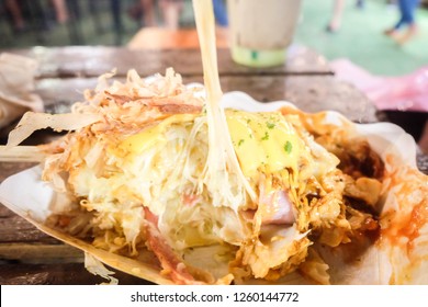 Okonomiyaki Pizza With Bacon And Cheese Stretch In Wooden Stick On A Paper Plate. Street Food. Japanese Pizza. Fat Food. High Calories. Cheese Pull. Food Market. Fair. Restaurant. Menu. 