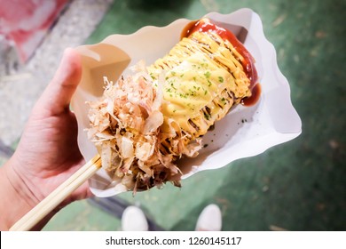 Okonomiyaki Pizza With Bacon And Cheese Stretch In Wooden Stick On A Paper Plate. Street Food. Japanese Pizza. Fat Food. High Calories. Cheese Pull. Food Market. Fair. Restaurant. Menu. 