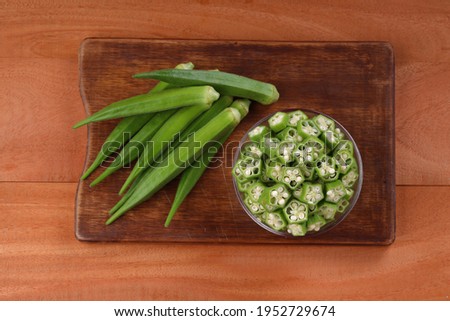  Okra or Lady's finger or Bhindi fresh green vegetable arranged  on a wooden board with a glass bowl full of okra sliced rings  with wooden background, selective focus ,top view.