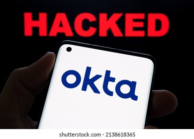 Okta security firm logo seen on smartphone hold in hand and the word HACKED on blurred background. Concept for hack. Stafford, United Kingdom, March 22, 2022.