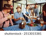 Oktoberfest joy. Men and women, friends sitting at table at local bar, enjoying beer. Celebration with Bavarian traditions. Concept of Oktoberfest, festival, party, brewery, traditions