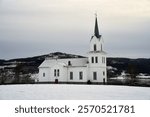 Olberg Church during a winter day. This timber-framed cruciform church with a paneled white exterior was built between 1857–1859 on Noresund, replacing the medieval stave church