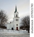 Olberg Church during a winter day. This timber-framed cruciform church with a paneled white exterior was built between 1857–1859 on Noresund, replacing the medieval stave church