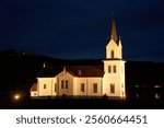 Olberg Church illuminated during the evening blue hour. This timber-framed cruciform church with a paneled white exterior was built between 1857–1859 on Noresund, replacing the medieval stave church