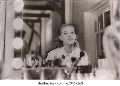 Old 1940s sepia photo of dreamy young woman looking in theater mirror.