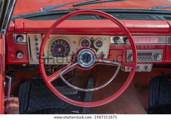 An old 1960s red convertible. View of the red\
steering wheel, automatic push button transmission and gauges on\
the dashboard.