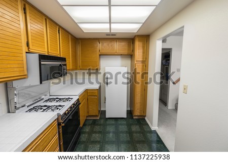 Old 1980s condo kitchen with oak cabinets, tile countertops, gas stove and green flooring. 