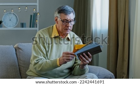 Old 60s elderly Caucasian man checking sorting letters in living room concentrated mature grandfather sitting on sofa looking at correspondence notice bank account aged pensioner check bills postal