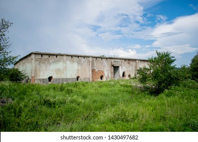 an old abandoned building located green grass field   Former warehouse fruits   vegetables in the 1980s  Holes in the walls   brick construction  beautiful blue sky and many fluffy clouds 