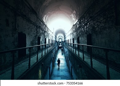 An old abandoned cell blocks in Eastern State Penitentiary, people walking to the light at the end of the dark tunnel