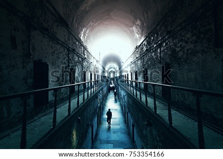 An old abandoned cell blocks in Eastern State Penitentiary, people walking to the light at the end of the dark tunnel
