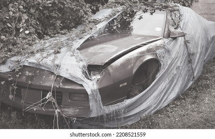 Old Abandoned Classic Sports Car In Need Of Repairs For Background Presentation In The Automotive Industry. The Vehicle Is Covered With A Torn Tarpaulin Sheet On The Side Road In Nature