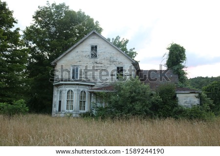 Old abandoned historic wooden farmhouse surrounded by weeds and overgrown field