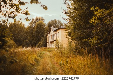 An old abandoned house stands in the middle of a dry autumn forest on a cloudy day. A sad abandoned place.