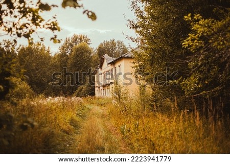 An old abandoned house stands in the middle of a dry autumn forest on a cloudy day. A sad abandoned place.