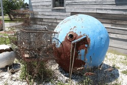 Old Abandoned Industrial Fishing Equipment Consisting Of Crab Traps And A Large Blue And White Buoy, Next To A Wooden Building