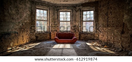 Old and abandoned room with three big broken windows and a red couch