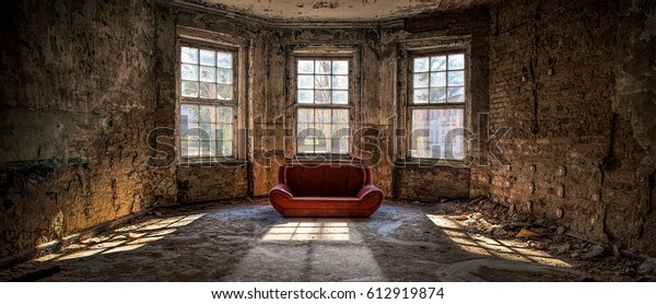 Old and abandoned room with three big broken\
windows and a red couch