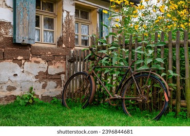 Old abandoned rusty bicycle leaning at a wooden fence in front of an old farm house - Powered by Shutterstock