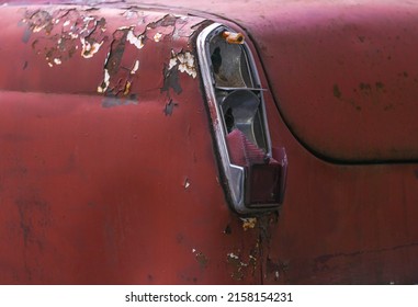 An old, abandoned, rusty, vintage car on the street.The broken taillight of an old car abandoned on a city street.A fragment of a broken taillight and cracked paint of a retro car.Corrosion of metal.