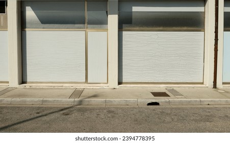 Old abandoned shop with white washed store windows at the road side. Concrete sidewalk and street in front. Background for copy space. - Shutterstock ID 2394778395