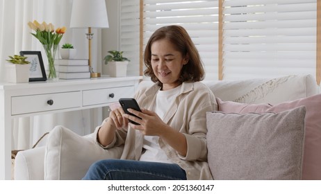 Old adult asia female sit relax on sofa couch smile watch, play, text chat on cellphone at home in happy retired in older people, elderly health care tech life, enjoy pay money online via banking app.
