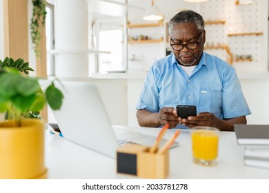 An old African man is sitting at his home office and using his phone and checking on e-mail.