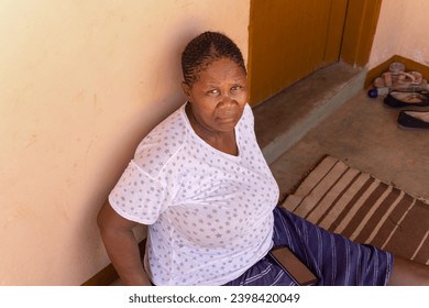 old african woman with braids hairstyle sited in front of the house holding her phone, village in botswana - Powered by Shutterstock