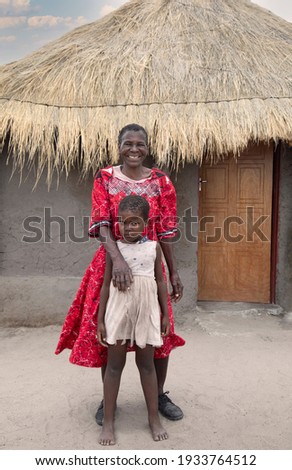old African woman and her granddaughter standing in her yard in a village in Botswana