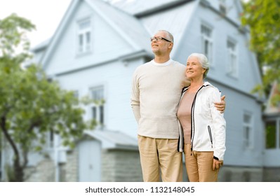 Old Age, Accommodation And Real Estate Concept - Happy Senior Couple Hugging Over House Background