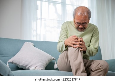 Old age. Asian senior man retirement knee joint pain on sofa, Elderly old man sitting down hands hold knee, Grandfather people health care bone problem at home - Powered by Shutterstock