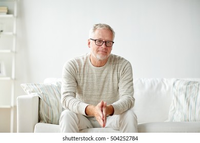 Old Age, Comfort And People Concept - Smiling Senior Man In Glasses Sitting On Sofa At Home