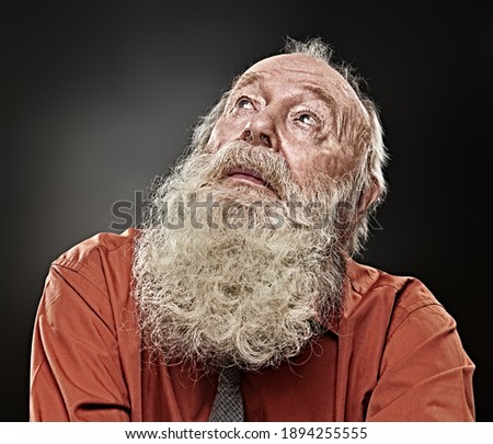 Old age concept. Portrait of an old man with white beard looking up expectantly. Black background. Religion and belief in God.