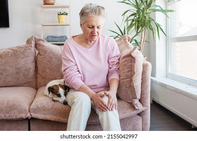old age, health problem and people concept - senior woman suffering from pain in leg. Elderly woman on sofa at home - Powered by Shutterstock