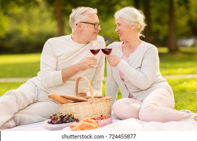 old age, holidays, leisure and people concept - happy senior couple with picnic basket and wine glasses sitting on blanket at summer park - Powered by Shutterstock