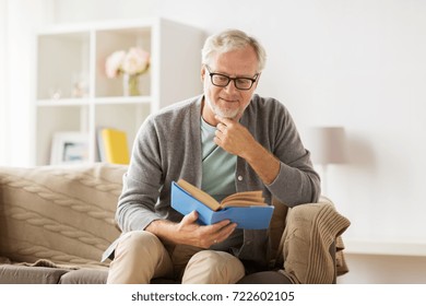 Old Age, Leisure And People Concept - Senior Man Sitting On Sofa And Reading Book At Home