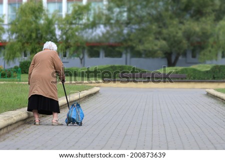 Old age - no joy. Old woman with bag seen from behind. Grandmother tired.