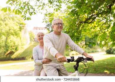 old age, people and lifestyle concept - happy senior couple riding together on bicycle at summer city park