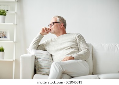 Old Age, Problem And People Concept - Senior Man In Glasses Thinking And Sitting On Sofa At Home