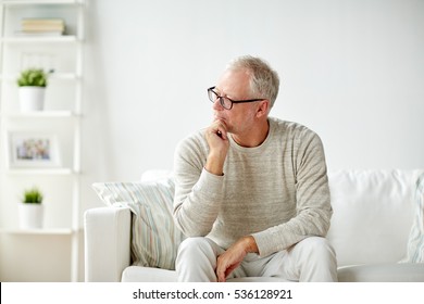 Old Age, Problem And People Concept -  Senior Man In Glasses Thinking And Sitting On Sofa At Home