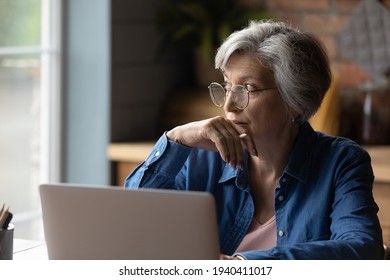 Old Age And Tech. Thoughtful Aged Latin Female Sit At Desk Work Online By Laptop From Home Office. Pensive Lady Retiree Learn To Use Internet Study Computer Ponder On Next Step Distracted From Screen