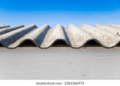 Old aged dangerous roof made of corrugated asbestos panels - one of the most dangerous materials in buildings and construction industry against sky