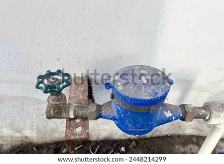 Old and aged dusty blue water pump and metal rusty faucet with green colored handle isolated on horizontal ratio grungy wall background.