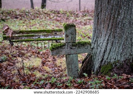old aged moss covered wooden cross and old bench on grave site in abandoned Latvia cemetery